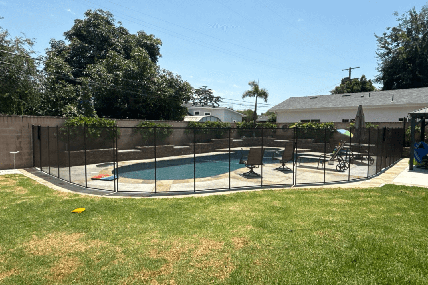 Black mesh pool fence surrounding a swimming pool and patio furniture set