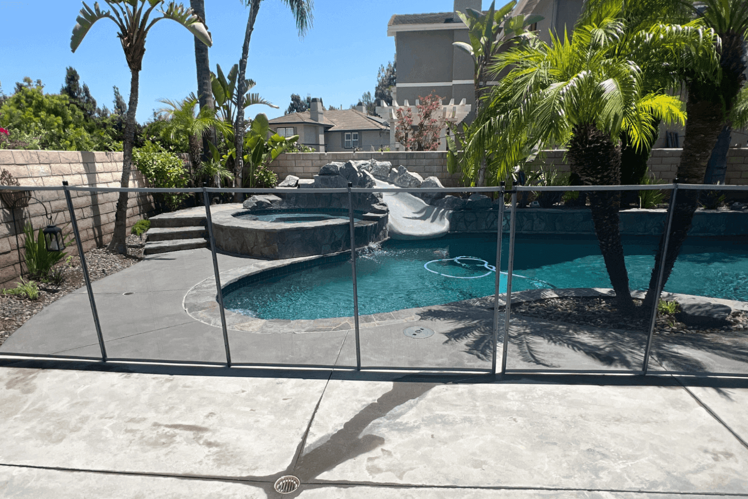 pool fence on concrete A concrete pool deck with palm tree landscaping and a mesh safety fence installed.
